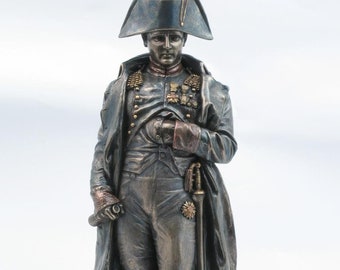 May include: A bronze statue of Napoleon Bonaparte in military uniform, wearing a bicorne hat and holding a sword. The statue is standing on a round base.