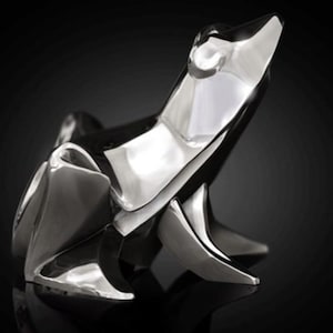 May include: A silver origami frog sculpture with a shiny, reflective finish. The frog is posed in a sitting position with its head tilted up.