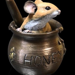 May include: A small, brown ceramic honey pot with a mouse peeking out of the top. The pot has the word "Honey" inscribed on the front.