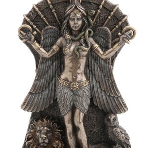 May include: A bronze-toned statue of a winged deity, holding ankhs, with a snake, and a starburst emblem. The figure has a feathered skirt, and is flanked by a lion and an owl. The statue is approximately 25 cm tall.