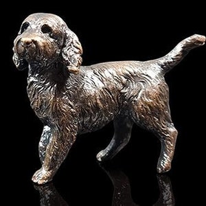 May include: A bronze sculpture of a brown and white Cocker Spaniel dog standing with its head turned to the side and its tail curled up.