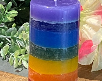 Könnte beinhalten: Eine mehrfarbige Kerze mit einer violetten oberen Schicht, blauen, grünen, gelben, orangen und roten Schichten. Die Kerze steht auf einer Holzoberfläche.