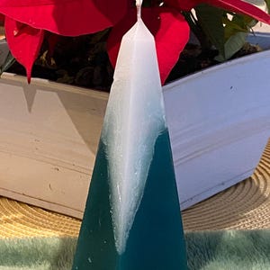 May include: A green and white pyramid-shaped candle. The candle is made of wax and has a white top with a green bottom.