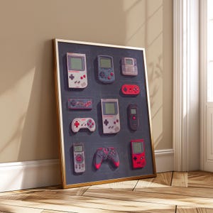 May include: A framed print featuring a collection of retro handheld gaming consoles and controllers. The artwork showcases various designs in a grid layout, with a dark blue background and a gold frame. The consoles are in shades of gray, red, and blue.