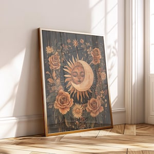 Può includere: Una stampa artistica incorniciata con un design celeste. L'opera raffigura una luna crescente con un volto sereno, circondata da un sole radioso ed elementi floreali, tra cui rose. La tavolozza dei colori include toni caldi di oro, arancione e marrone su uno sfondo scuro.