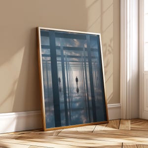 Puede incluir: Impresión artística enmarcada que presenta una escena surrealista. Una figura camina por un largo corredor con líneas verticales y horizontales, reflejándose en una superficie espejada. La obra de arte tiene un marco dorado y está apoyada contra una pared.