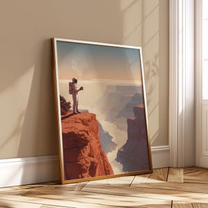 May include: Framed art print featuring an astronaut standing on a red rock cliff, holding a cup with steam rising. The artwork depicts a canyon landscape with a hazy atmosphere and a gold frame.