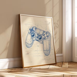 Peut inclure: Une affiche encadrée représentant un plan d'un contrôleur de jeu vidéo en encre bleue. Le contrôleur est détaillé avec des boutons et des joysticks, sur un fond beige. L'affiche est dans un cadre doré, appuyée contre un mur.