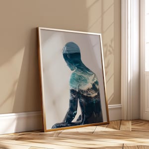 Puede incluir: Una impresión artística enmarcada que presenta una figura con un diseño de olas oceánicas azules y blancas. La obra de arte está en un marco dorado y se apoya contra una pared. La figura está en posición sentada, con las olas del océano incorporadas.