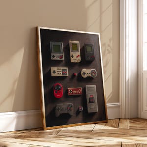 May include: A framed artwork featuring a collection of vintage video game consoles and controllers. The arrangement includes handheld consoles, controllers, and game cartridges in various colors, set against a dark wood-grain background with a gold frame.
