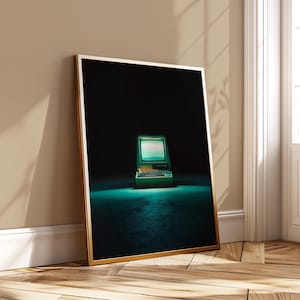 May include: Framed art print featuring a vintage computer with a glowing screen. The computer is green and gold, set against a dark background with a teal glow. The print is in a gold frame, leaning against a wall.
