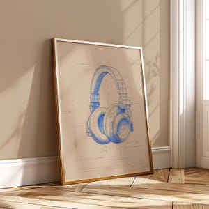 Peut inclure: Impression encadrée d'un dessin technique bleu de casque audio sur fond beige. Le casque est détaillé, avec des oreillettes et un bandeau visibles. Le cadre est doré et l'impression est appuyée contre un mur.
