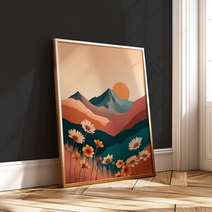 May include: A framed art print depicting a landscape with mountains, a setting sun, and wildflowers. The artwork uses orange, teal, and pink colours. The frame is gold-coloured.