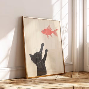 May include: Framed art print featuring a black cat reaching for a red fish. The cat is silhouetted against a light background, with its paws raised. The fish is depicted in a simple, stylized manner. The frame is gold-colored.