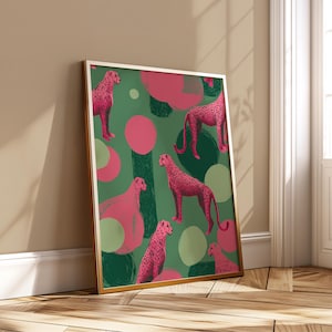 May include: Framed art print with a repeating pattern of pink cheetahs on a green background, with pink and green abstract shapes. The gold-coloured frame leans against a wall.