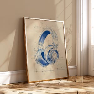 Peut inclure: Impression encadrée représentant un dessin de casque audio en style plan. L'œuvre est réalisée en bleu sur un fond beige, avec des lignes fines et des détails suggérant un dessin technique. Le cadre est doré.
