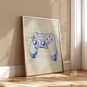 May include: Framed print featuring a blueprint-style illustration of a video game controller in blue ink. The controller is centered on a grid background, with a gold frame. The artwork is leaning against a wall.