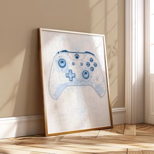 May include: A framed print featuring a blue and white schematic of a video game controller. The controller design is centered on a white background, with a gold frame. The print is leaning against a wall.