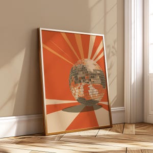 May include: A framed art print featuring a disco ball illustration. The artwork has a retro style with an orange and beige color scheme. The disco ball is in the center, with sunburst rays emanating from behind it.
