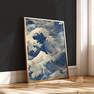 May include: A framed print featuring a stylized depiction of ocean waves in shades of blue and white. The artwork has a vintage aesthetic, with a gold-colored frame. The print is leaning against a dark wall.