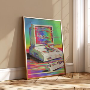May include: A framed art print depicting a retro computer and controller with a glitch effect. The artwork is in a gold frame and leans against a wall. The colour scheme includes white, green, blue, and red.