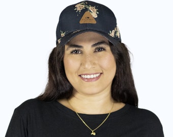 Op de afbeelding: Een vrouw draagt een zwart T-shirt met een baseballpet met bloemenprint. De pet heeft een bruin leren patch met de tekst "EXTRNCE SINCE 1992".