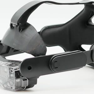 May include: Black VR headset with a clear lens and adjustable straps. The headset has a sleek, modern design. The clear lens reveals internal components. The design focuses on comfort and functionality.