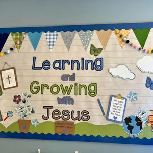 May include: A rectangular bulletin board with a blue scalloped border featuring the text Learning and Growing with Jesus. Decorations include fabric bunting, felt balls, butterflies, clouds, a backpack, a potted plant, a globe, and books.