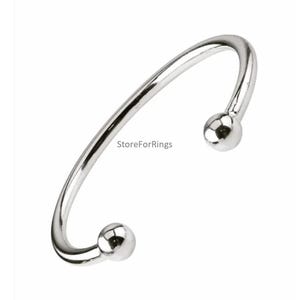 Könnte beinhalten: Ein silbernes Armreif-Armband mit zwei runden Kugelenden.