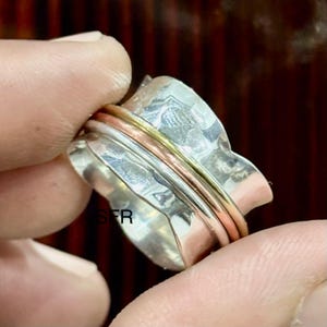 Peut inclure: Une bague tournante en argent avec deux bandes de cuivre et d'or. La bague est texturée et a une finition martelée.