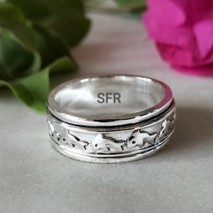 Könnte beinhalten: Ein silberner Drehring mit einem Delfin-Design. Die Innenseite des Rings ist mit den Buchstaben "SFR" gekennzeichnet.