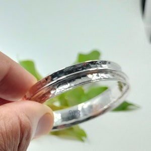 Peut inclure: Un bracelet jonc en métal argenté présentant une surface martelée et texturée avec une finition réfléchissante. L'anneau circulaire possède une rainure centrale distincte le long de sa circonférence. Les lettres SFR sont imprimées en bleu.
