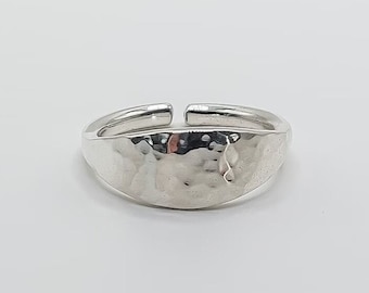 May include: A silver ring with a hammered, oval-shaped band. The ring is open on one side, making it adjustable.