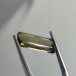 May include: A faceted, rectangular, brown and green gemstone held by tweezers.