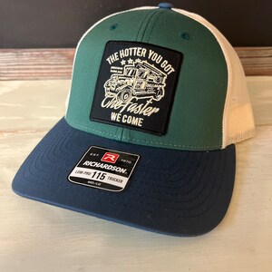 May include: A green and white trucker hat with a black patch that says "The hotter you go the faster we come" with a cartoon image of a truck. The hat also has a red and white label that says "Richardson 115 Trucker".