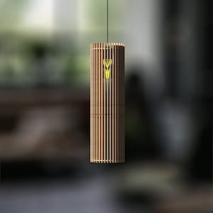 Op de afbeelding: Een houten hanglamp met een cilindrische kap gemaakt van dunne, verticale latten. De lamp is aan en straalt een warm, geel licht uit.