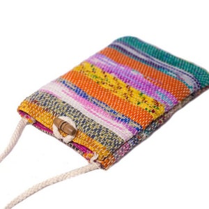 Puede incluir: Un bolso bandolera tejido a rayas de colores con cierre de botón de madera y correa de algodón blanco.