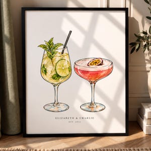 Peut inclure: Une impression d'art encadrée représentant deux cocktails à l'aquarelle. L'un est dans un verre haut avec du citron vert et de la menthe, l'autre dans une coupe avec un fruit de la passion. Le texte indique ELIZABETH & CHARLIE EST. 2012.