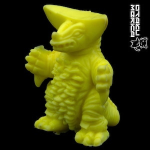 May include: A bright yellow, stylized monster figure with a large head crest, textured body, and outstretched arms. The figure has a dinosaur-like appearance and is set against a black background. The image includes the text "STEKU MORIKA" in white.