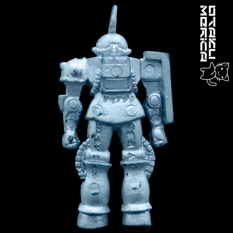 K&ouml;nnte beinhalten: Hellblaue Spielzeug-Roboterfigur mit Schild und einzelner Antenne. Der Roboter hat detaillierte mechanische Merkmale und japanischen Text auf Beinen und Torso. Der Hintergrund ist tiefschwarz.