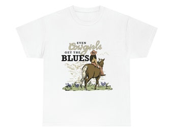 Puede incluir: Camiseta blanca con un gráfico de una vaquera montando un caballo con el texto "Even Cowgirls Get the Blues".