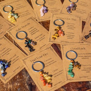 May include: A collection of keychains with various colorful gemstone clusters. Each keychain is attached to a card with text, including phrases like "Clear Vision" and "Good Luck." The keychains are arranged on a wooden surface.