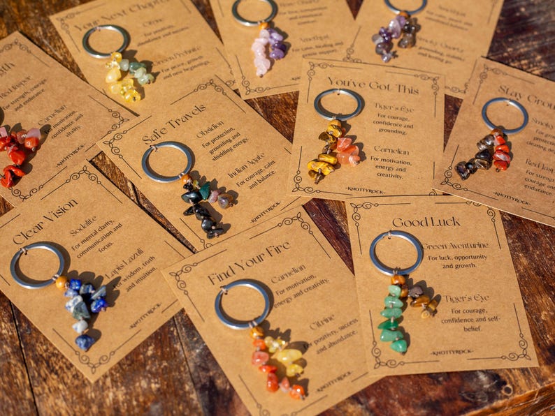 May include: A collection of keychains with various colorful gemstone clusters. Each keychain is attached to a card with text, including phrases like "Clear Vision" and "Good Luck." The keychains are arranged on a wooden surface.