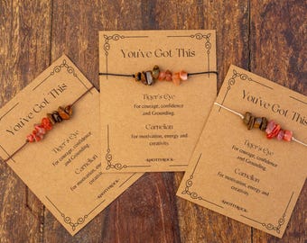 May include: Three gemstone bracelets with Tiger's Eye and Carnelian beads are displayed on cards that read "You've Got This." The cards are brown with decorative borders and text. The bracelets are strung on cords.