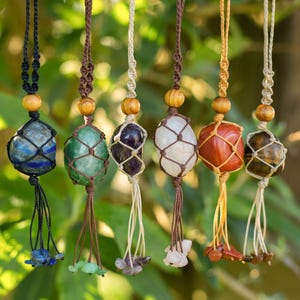 May include: Seven gemstone pendants, each held in a macrame net and hung from a knotted cord. The gemstones are in various colours, including blue, green, purple, white, red, and brown. Wooden beads are on the cords, and each pendant has a tassel.