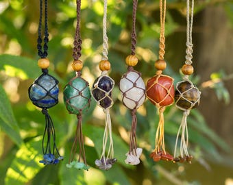 May include: Seven gemstone pendants, each held in a macrame net and hung from a knotted cord. The gemstones are in various colours, including blue, green, purple, white, red, and brown. Wooden beads are on the cords, and each pendant has a tassel.