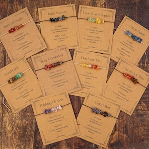 May include: A collection of gemstone bracelets displayed on kraft paper cards. Each card features a different bracelet with a unique combination of colorful stones and text such as "Inner Strength" and "Good Luck". The bracelets are strung on thin cords.