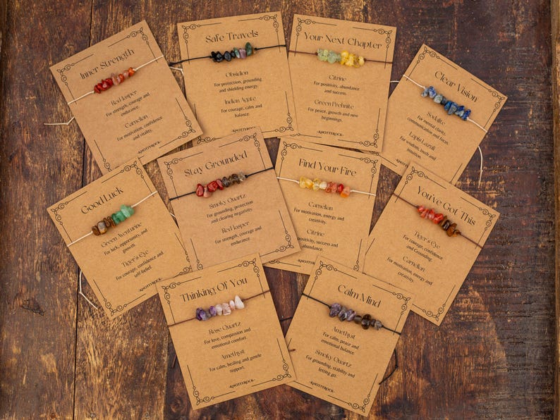 May include: A collection of gemstone bracelets displayed on kraft paper cards. Each card features a different bracelet with a unique combination of colorful stones and text such as "Inner Strength" and "Good Luck". The bracelets are strung on thin cords.