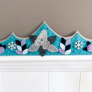 May include: A turquoise felt crown with a silver glitter number four, white and purple felt flowers, black felt leaves, and silver glitter snowflakes.