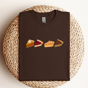 May include: A brown t-shirt with a graphic of four different slices of pie. The pies are pumpkin, cherry, apple, and pecan.